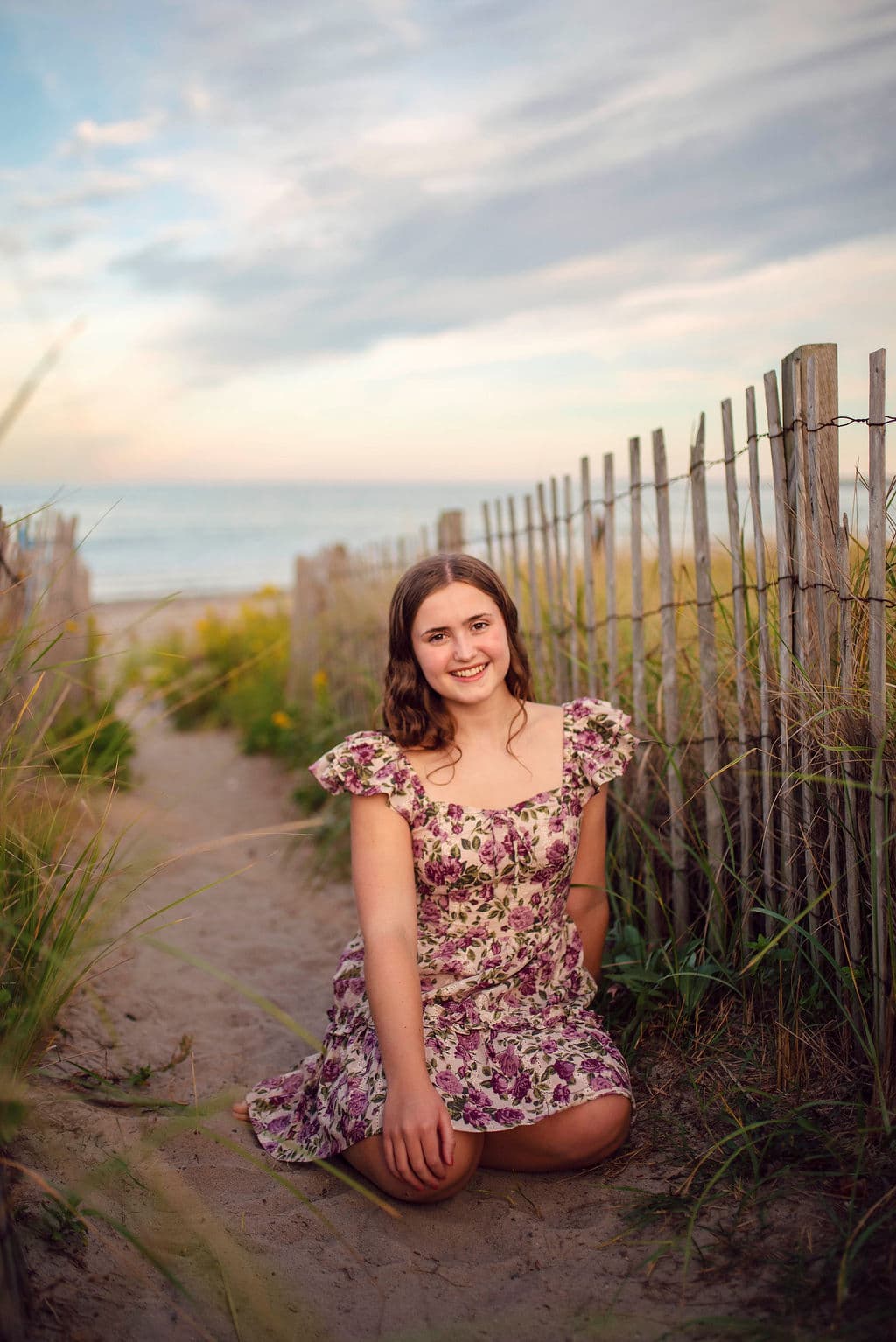Senior girl in a floral dress on a sandy dune path by the sea