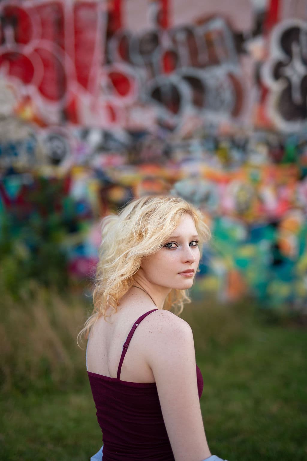 Senior girl looking over her shoulder in front of a colorful graffiti wall