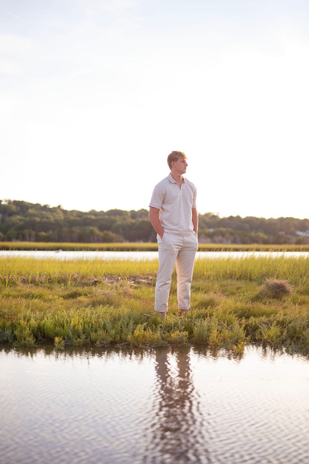 Senior guy standing in a salt marsh with his reflection in the water