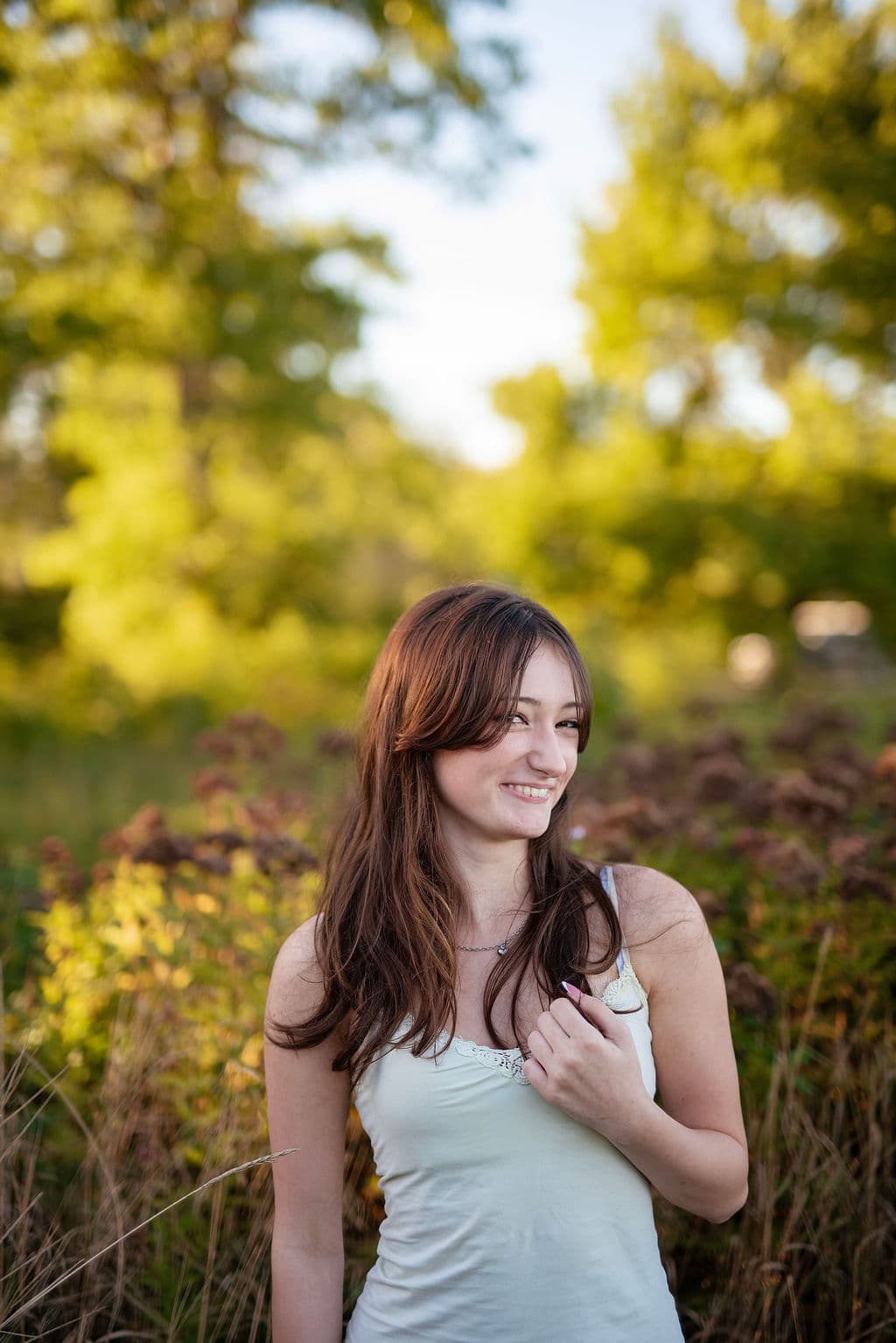 Smiling senior girl surrounded by summer wildflowers in soft natural light